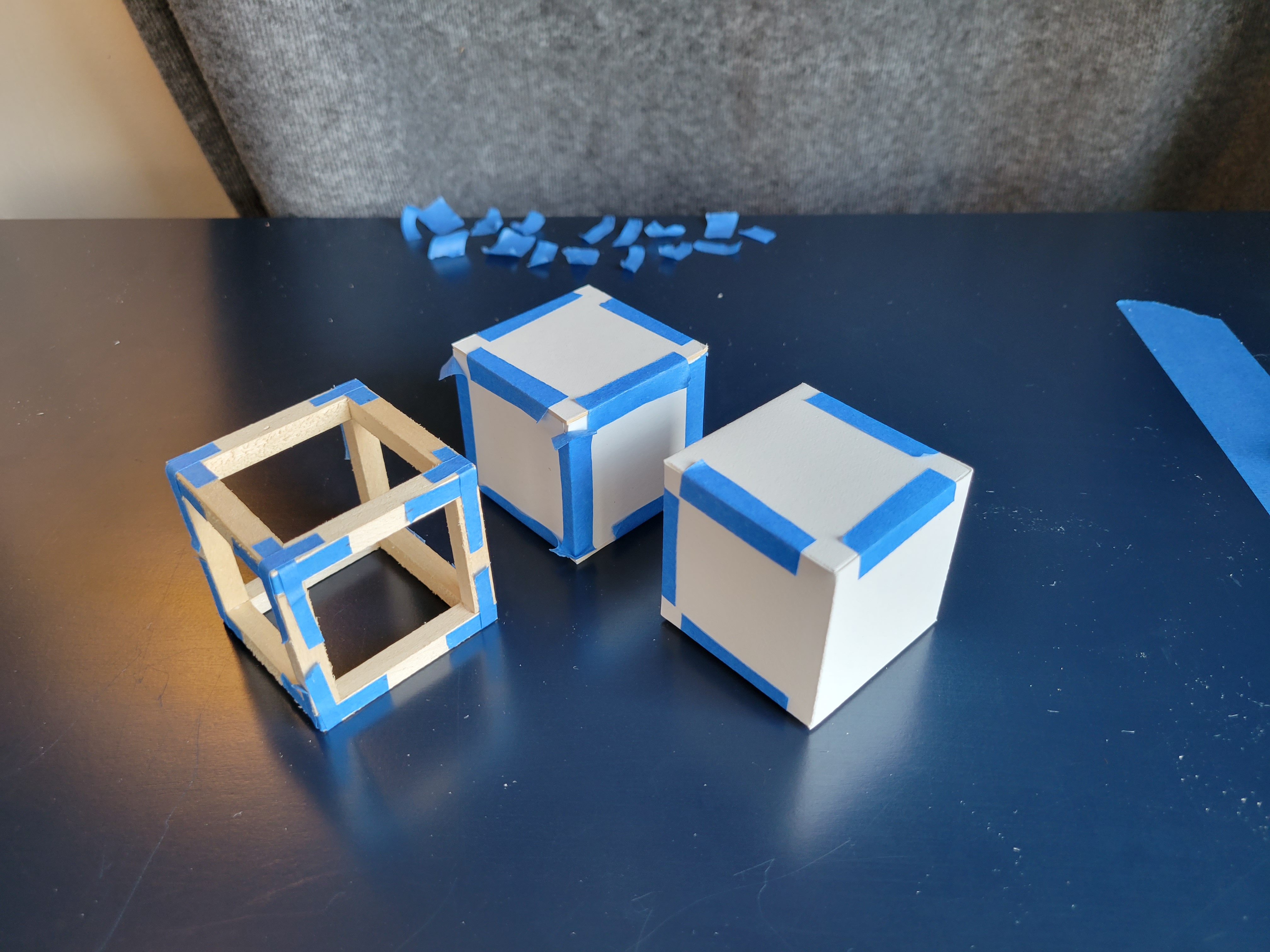 Photograph of three model cubes joined with tape. One cube is paper, another is illustration board, and the third is wood.
