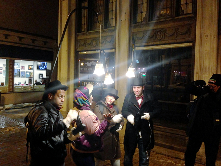 Three service artists providing light with hanging lamp harnesses to viewer on sidewalk.