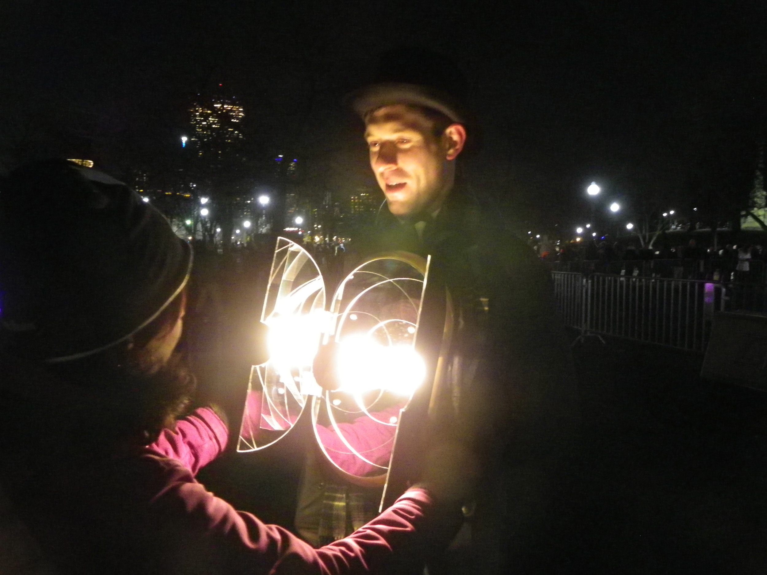 Service artist wearing illuminated mirror harness speaking with viewer looking at self in mirror.