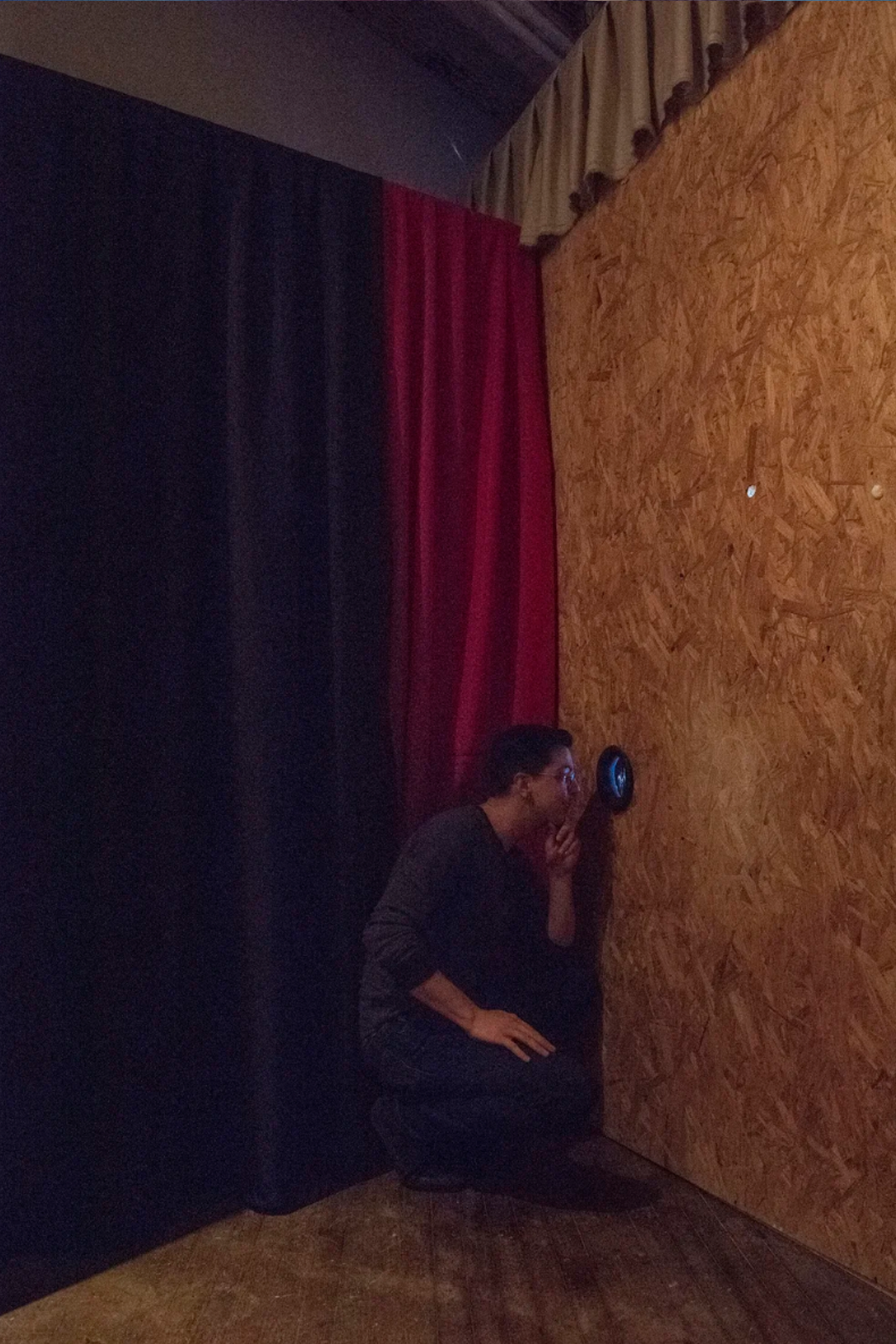 Opening night photograph of viewer looking through hole cut in plywood wall.