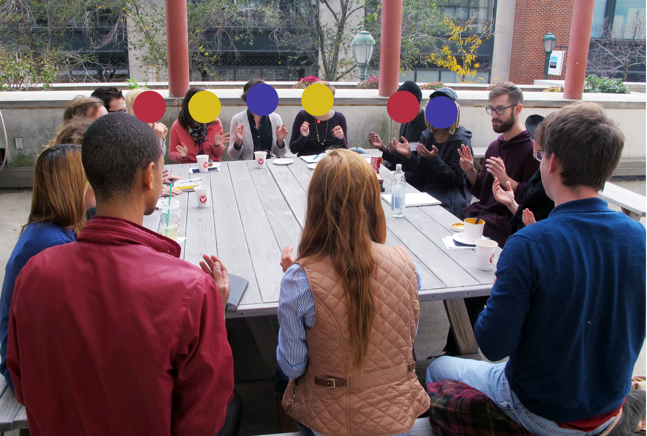Portrait of Keenan Jackson leading a conversation around a wooden table outdoors.